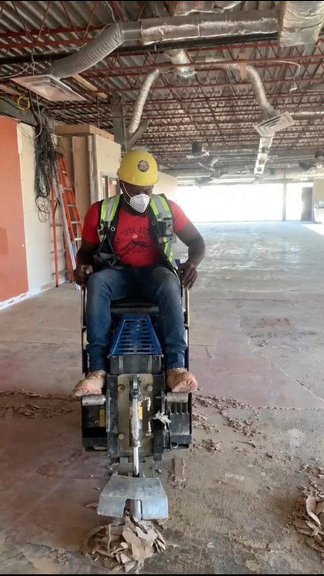 Crew member on a ride-on floor stripping machine in an open commercial space