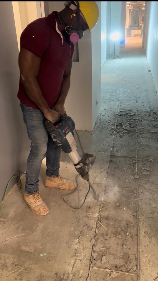 Crew member using a breaker hammer in a finished hallway, in a mask and hard hat