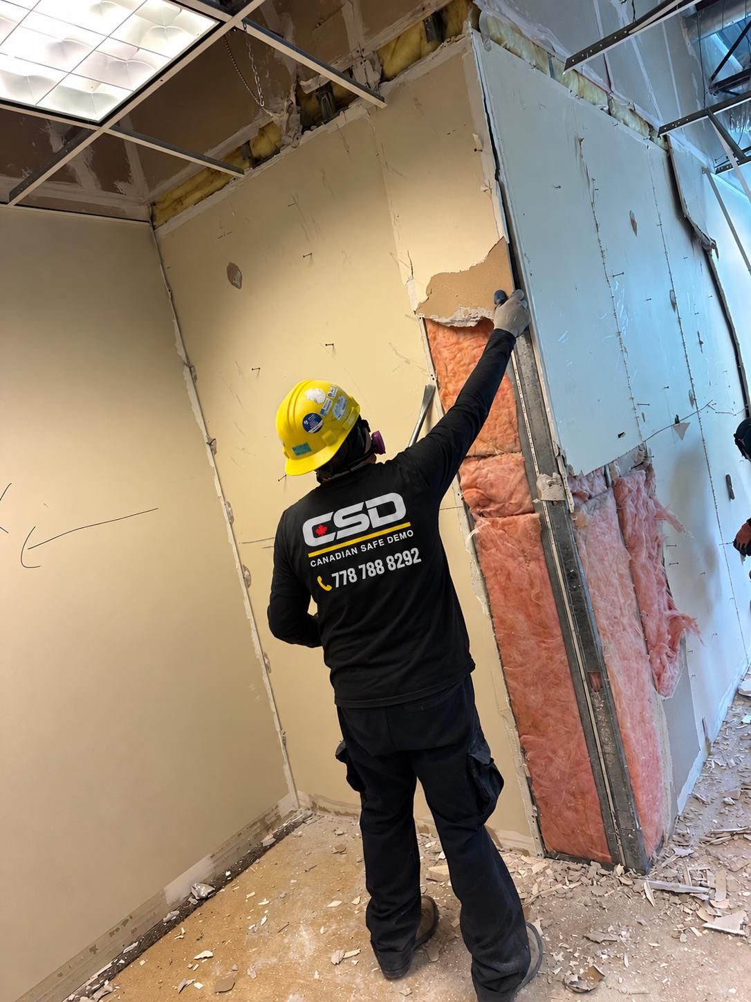 Worker removing drywall and exposing pink insulation and metal studs in a Vancouver commercial space