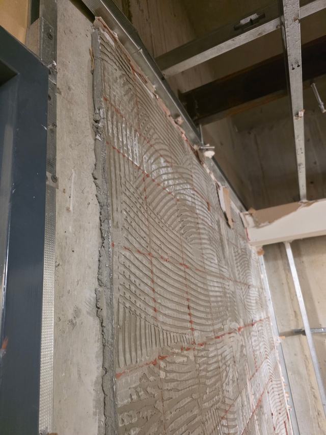 Tile bed removed from a concrete wall beside steel studs